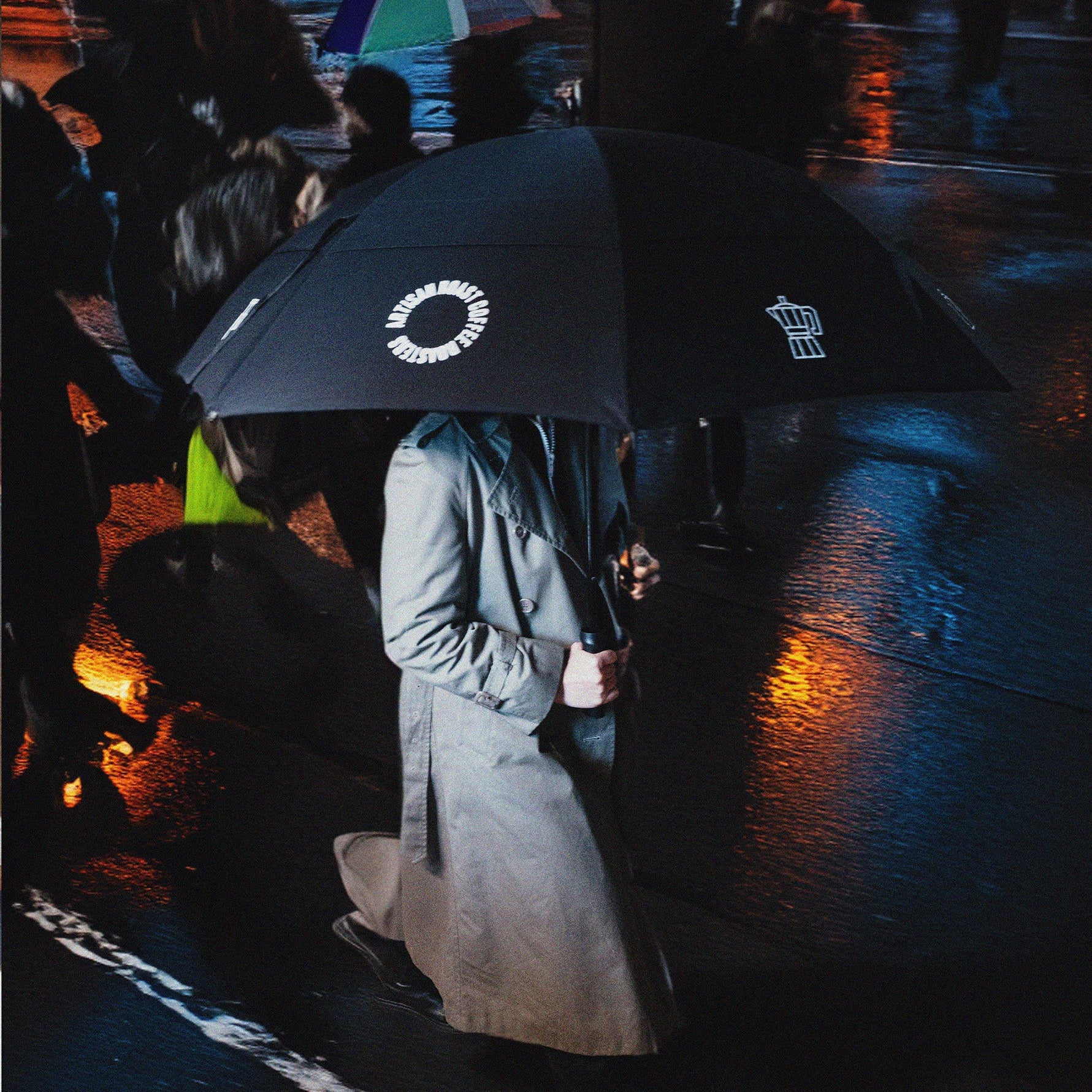 Person holding a black umbrella with visible branding on a rainy street.